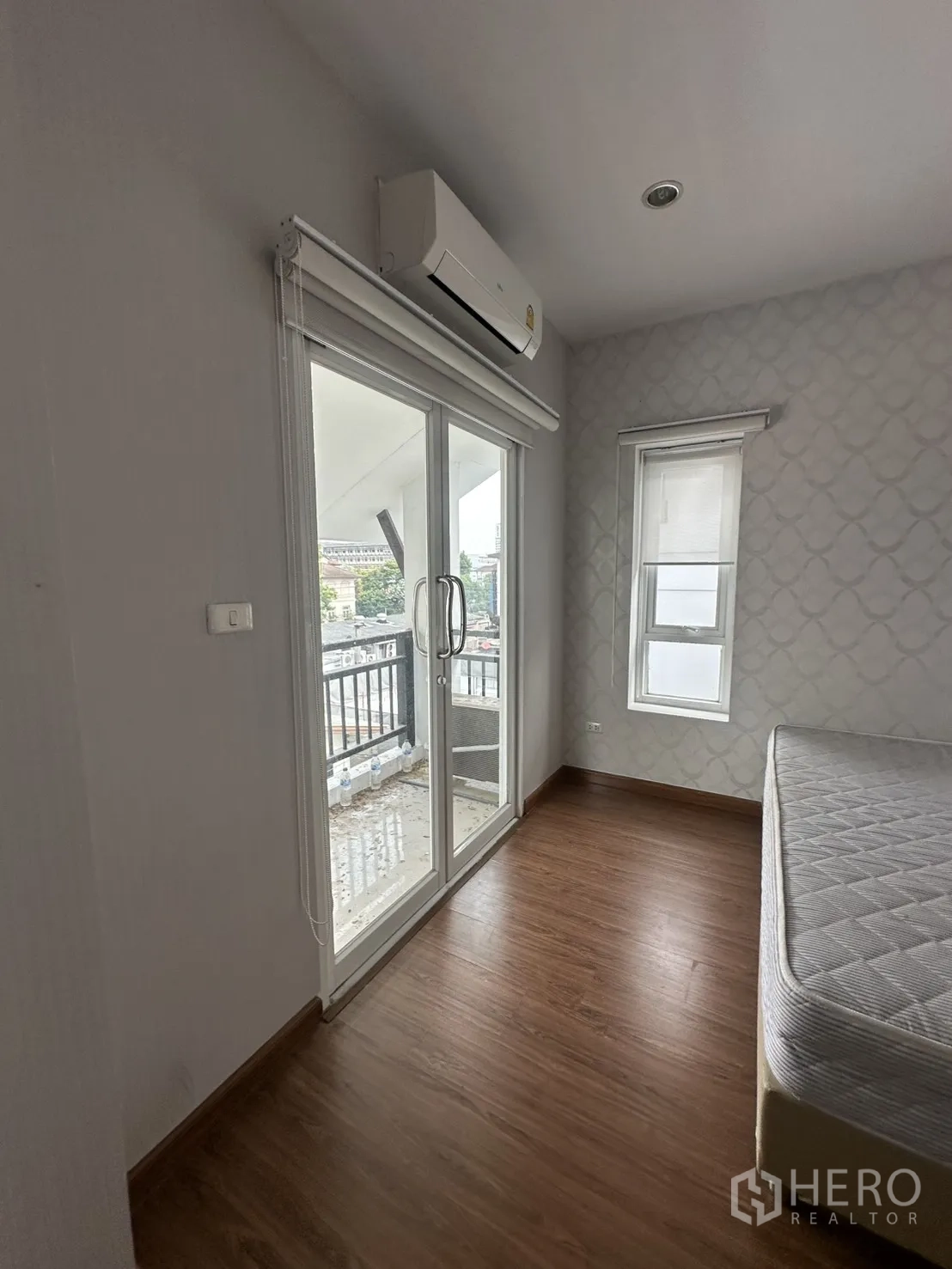 Home Office for rent in Watthana, Bangkok - Cozy bedroom with wood flooring, sliding glass door to a balcony, roller blinds and wall-mounted air conditioner.
