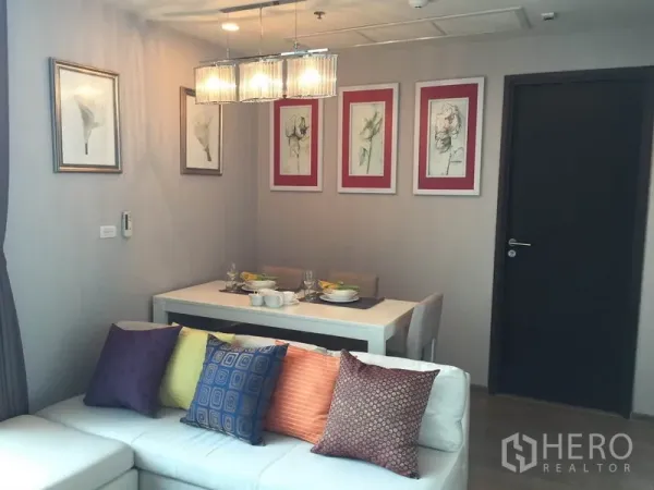 Condominium for rent in Ratchathewi, Bangkok - Living zone with sectional sofa and colorful cushions beside a bright dining table and wall art.