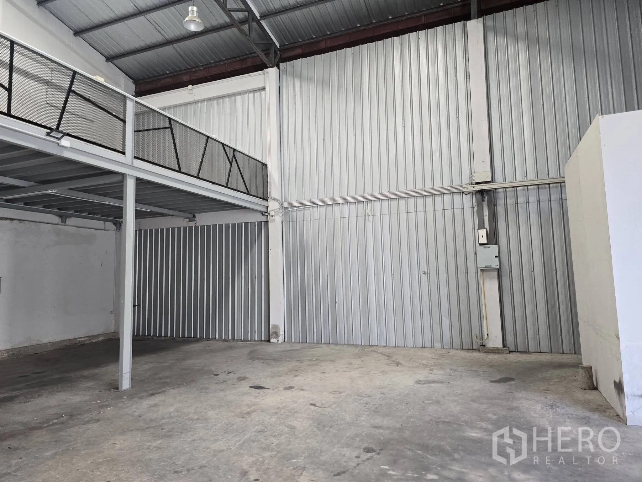 Warehouse for rent in Bang Na, Bangkok - Warehouse interior with concrete floor, tall metal cladding walls, mezzanine with mesh railing, and wide shutter door.