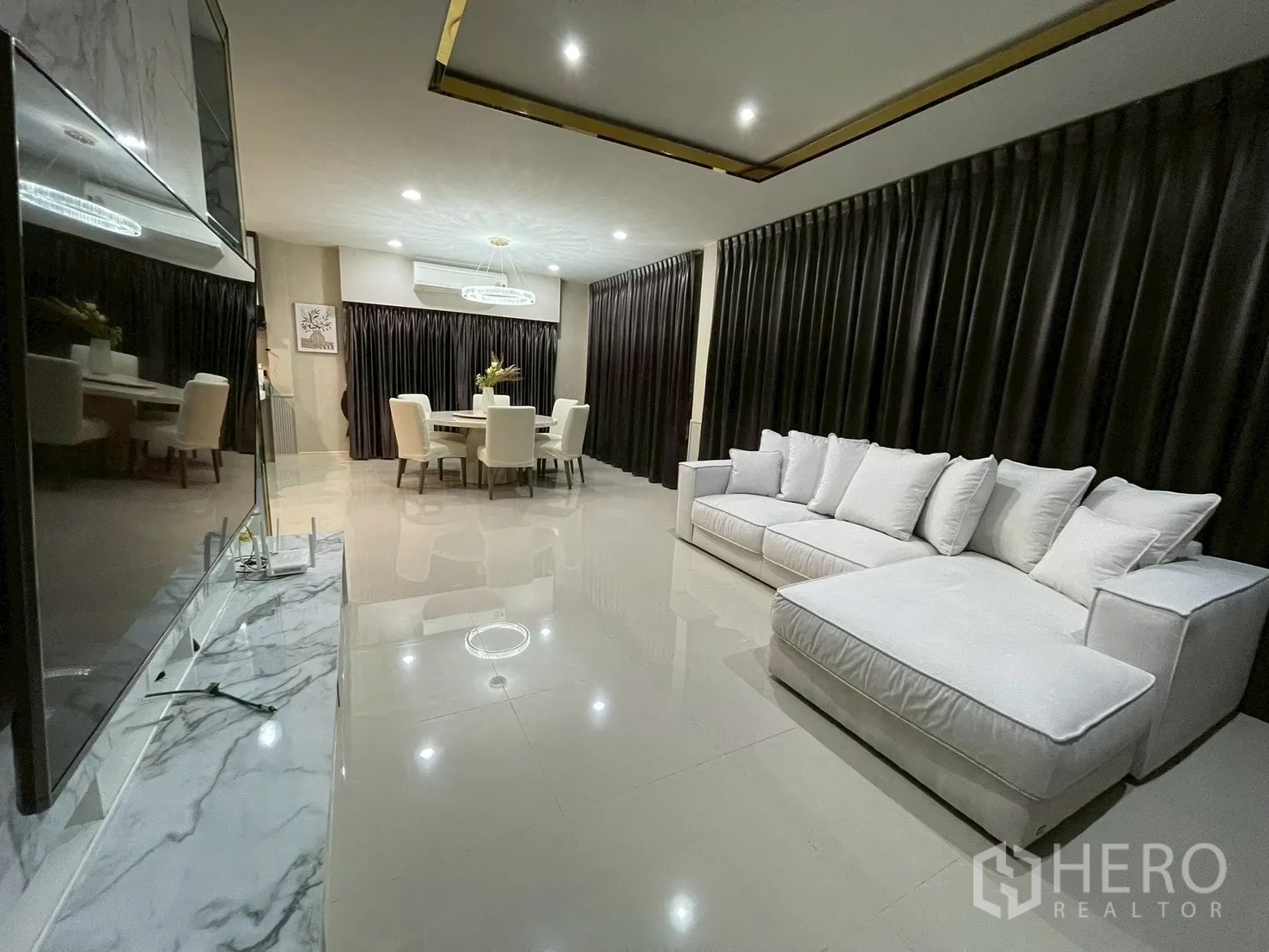 Detached House for rent in Bang Kapi, Bangkok - Open-plan living room with white sectional sofa and full-length curtains.
