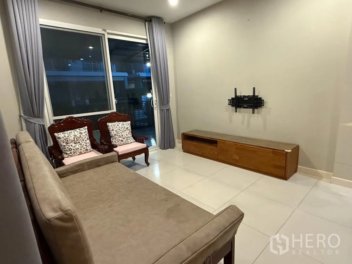 Detached House for rent in Bang Na, Bangkok - Living room wall with TV mount, low cabinet and large window with drapes.