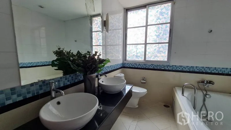 Condominium for rent in Khlong Toei, Bangkok - Master bathroom with double sinks, long countertop, bathtub, and blue mosaic accents.