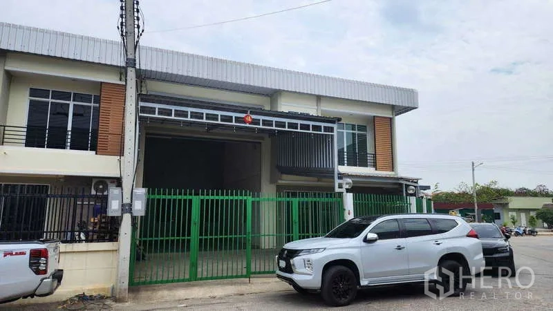 Factory for rent in Samut Sakhon - Modern two-storey factory exterior with green gate, parking and wide driveway.