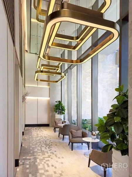 Condominium for rent or sale in Pathum Wan, Bangkok - High-ceiling lobby with contemporary gold chandeliers, lounge seating, and tall windows.