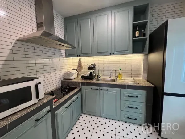 独立式住宅 出售在Bang Kruai, Nonthaburi - L形厨房，灰蓝色橱柜、抽油烟机、砖墙防溅板和电器。