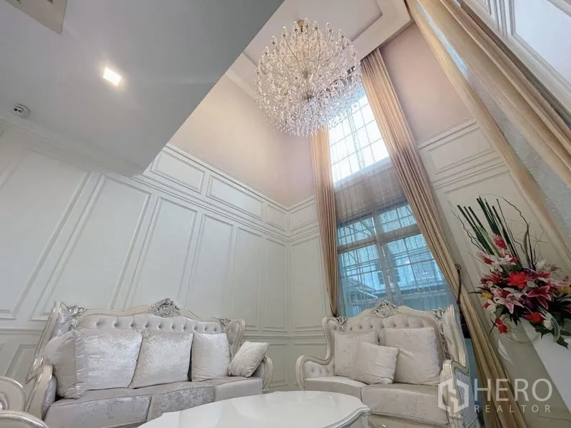 Detached House for rent or sale in Bang Phli, Samut Prakan - Double‑height lounge featuring a crystal chandelier, tall windows, and white wall paneling.