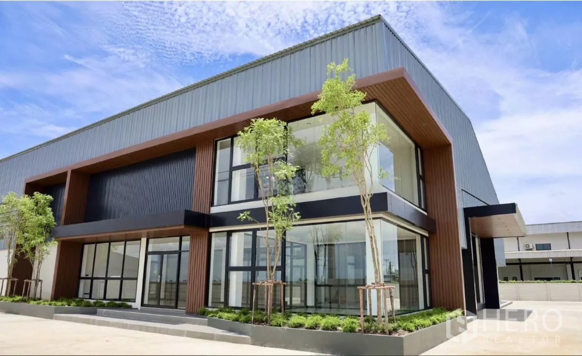 工厂 出租或出售在Phutthamonthon, Nakhon Pathom - 近景展示挑高入口、转角落地玻璃与景观花坛。