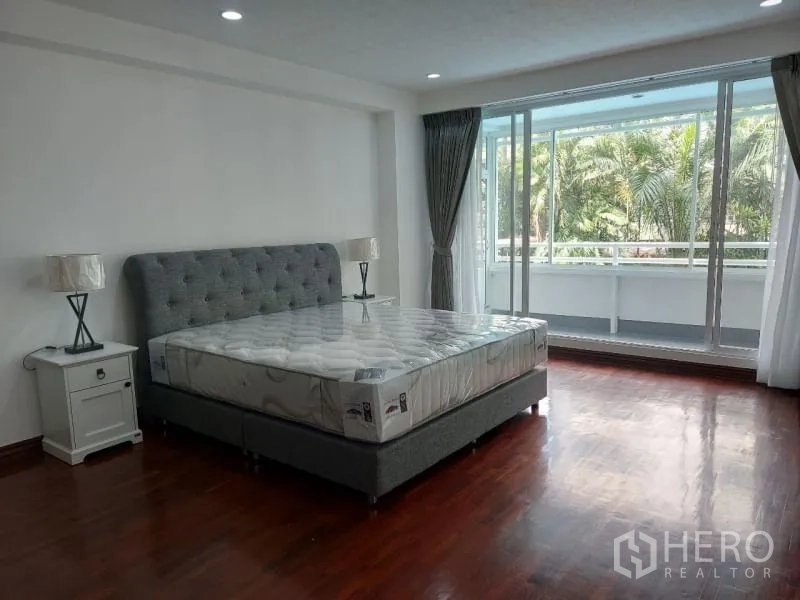 คอนโด ให้เช่าในWatthana, Bangkok - ห้องนอนสว่าง เตียงหัวเตียงบุตะเข็บ และประตูกระจกบานใหญ่เปิดออกสู่ระเบียงมองเห็นต้นปาล์ม