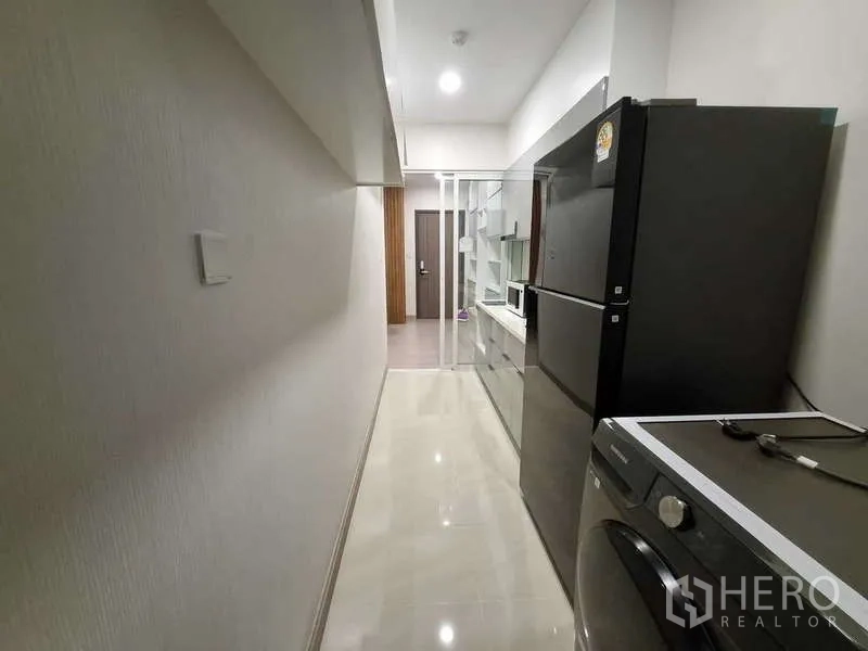 公寓 出租 - 狭长厨房走道，前景为冰箱和洗衣机，望向入户门。