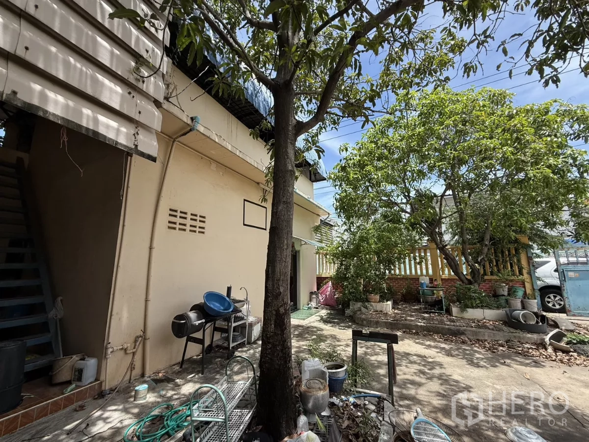 Warehouse for sale in Phra Samut Chedi, Samut Prakan - Utility side yard with mature trees, planters and outdoor sink along the building wall.