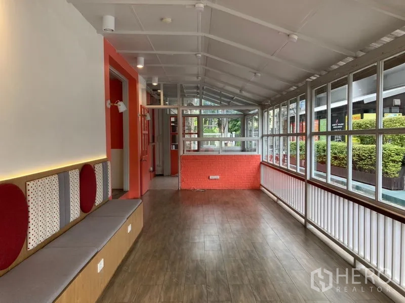 零售空间 出租在Khlong Toei, Bangkok - 通透的玻璃长廊式店铺，轨道灯与橙色点缀，外望绿植景观。