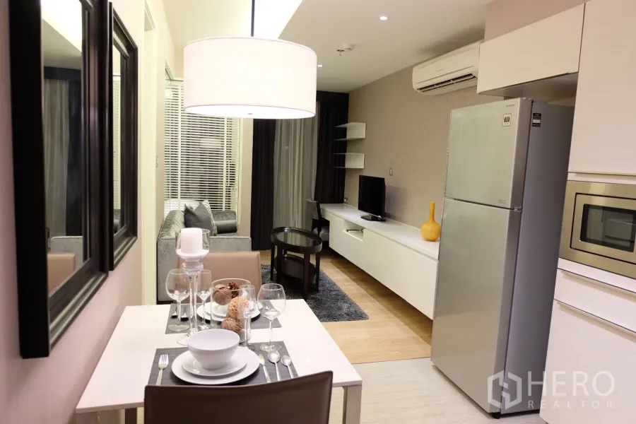Condominium for rent in Watthana, Bangkok - Intimate dining area set for two beside an open-plan living room and kitchen in neutral tones.