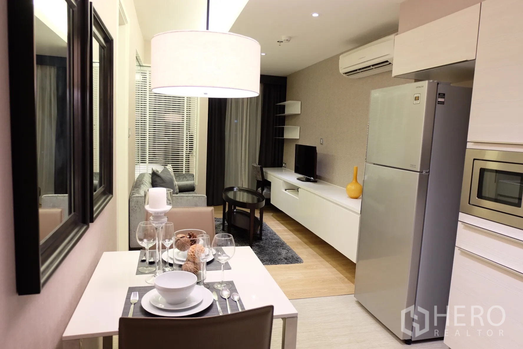 Condominium for rent in Watthana, Bangkok - Intimate dining area set for two beside an open-plan living room and kitchen in neutral tones.