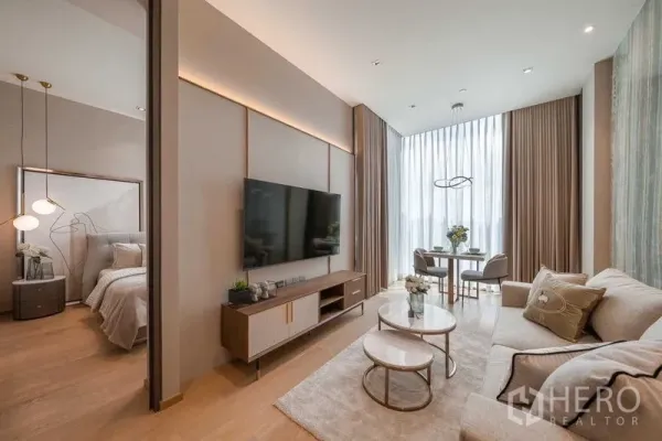 Condominium for rent or sale in Pathum Wan, Bangkok - Open-plan living area with TV wall, nesting coffee tables and dining by floor-to-ceiling curtains.