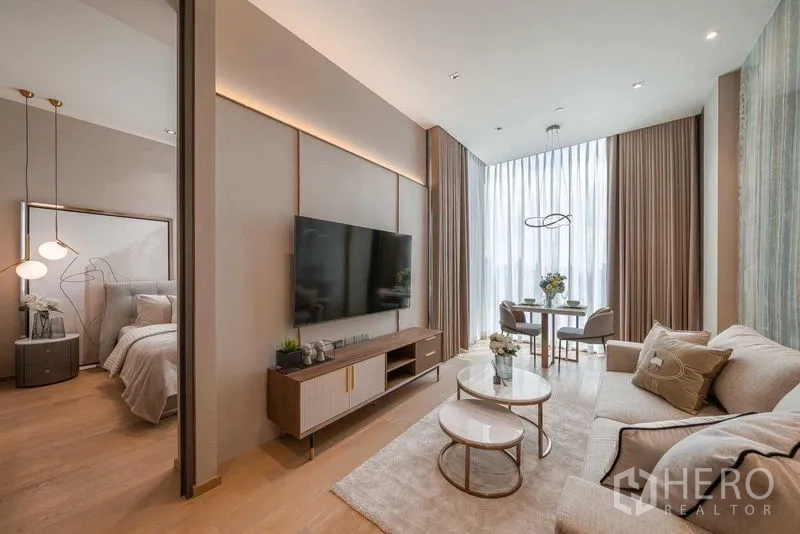 Condominium for rent or sale in Pathum Wan, Bangkok - Open-plan living area with TV wall, nesting coffee tables and dining by floor-to-ceiling curtains.