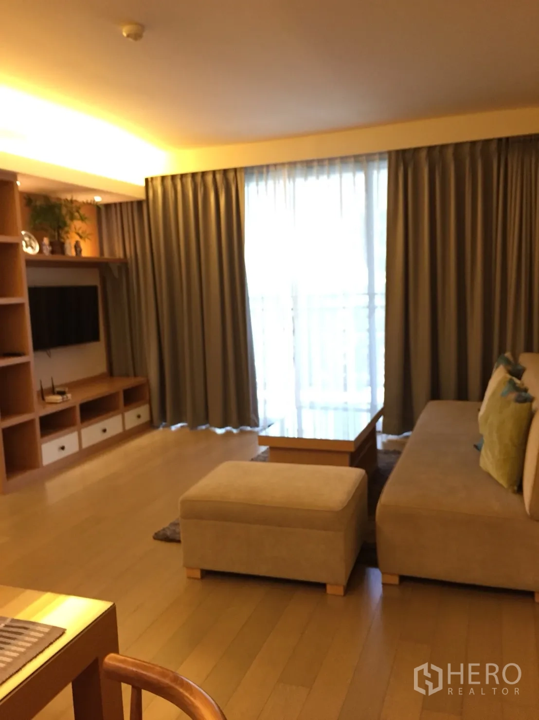 Condominium for rent in Watthana, Bangkok - Bright living room with sofa, ottoman, built-in TV shelving and full-length curtains.