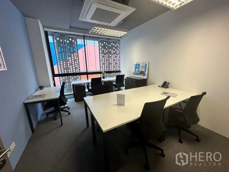 Office Space for rent - Compact private office with white desks, meeting table, carpet flooring and large window with dotted privacy film in Khlong Toei, Bangkok.