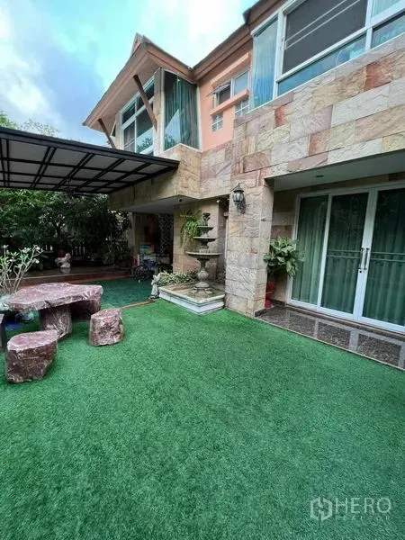 Detached House for sale in Bueng Kum, Bangkok - Private garden with artificial lawn, stone facade, sliding glass doors, and covered patio.