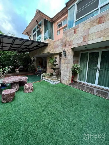 Detached House for sale in Bueng Kum, Bangkok - Private garden with artificial lawn, stone facade, sliding glass doors, and covered patio.