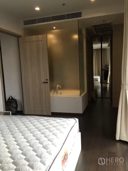 Condominium for rent in Watthana, Bangkok - Bedroom leading to ensuite with frosted-glass bathtub partition, wood door, and mirrored wardrobe.