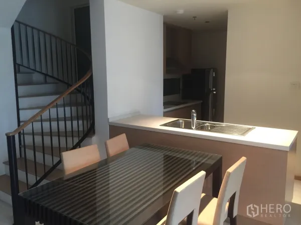 Condominium for rent in Sathon, Bangkok - Duplex condo interior with spiral staircase beside an open kitchen island and glass-top dining table.