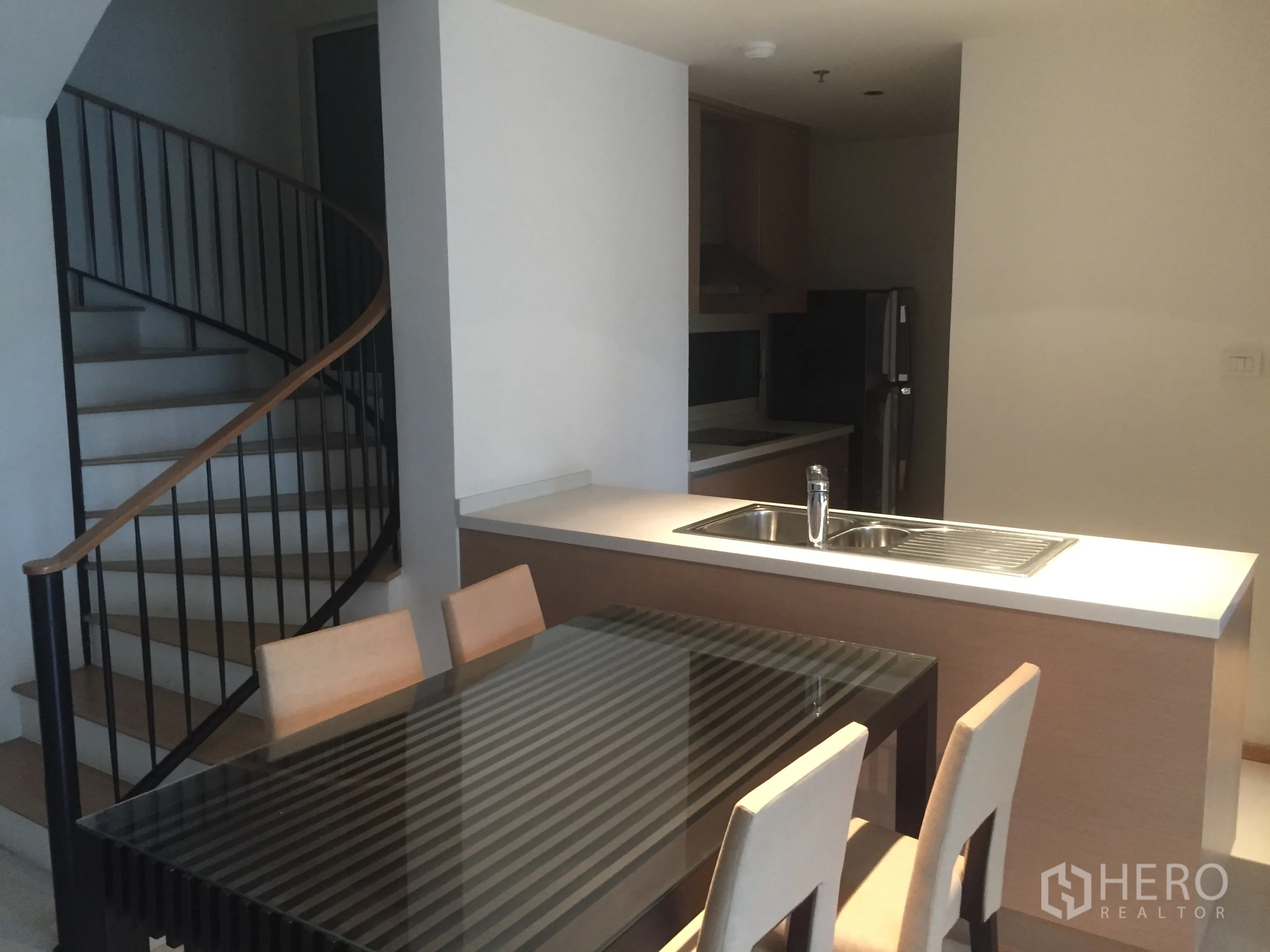 Condominium for rent in Sathon, Bangkok - Duplex condo interior with spiral staircase beside an open kitchen island and glass-top dining table.