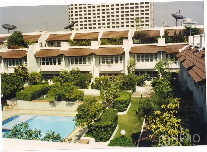 Townhouse for rent or sale in Watthana, Bangkok - Townhouse community exterior with landscaped gardens and a central swimming pool.