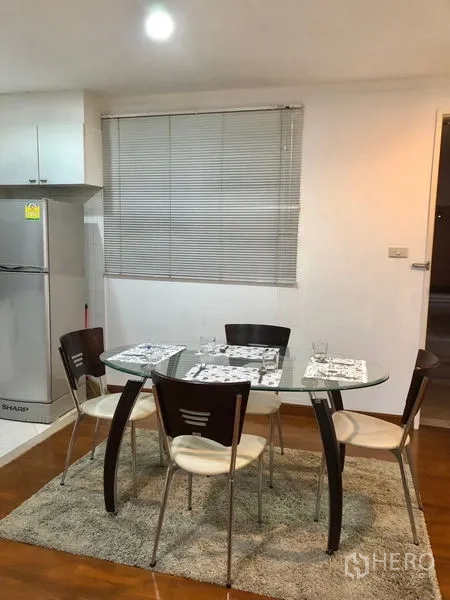 Condominium for rent or sale in Watthana, Bangkok - Dining nook with round glass table, four chairs, and window blinds beside the kitchen.