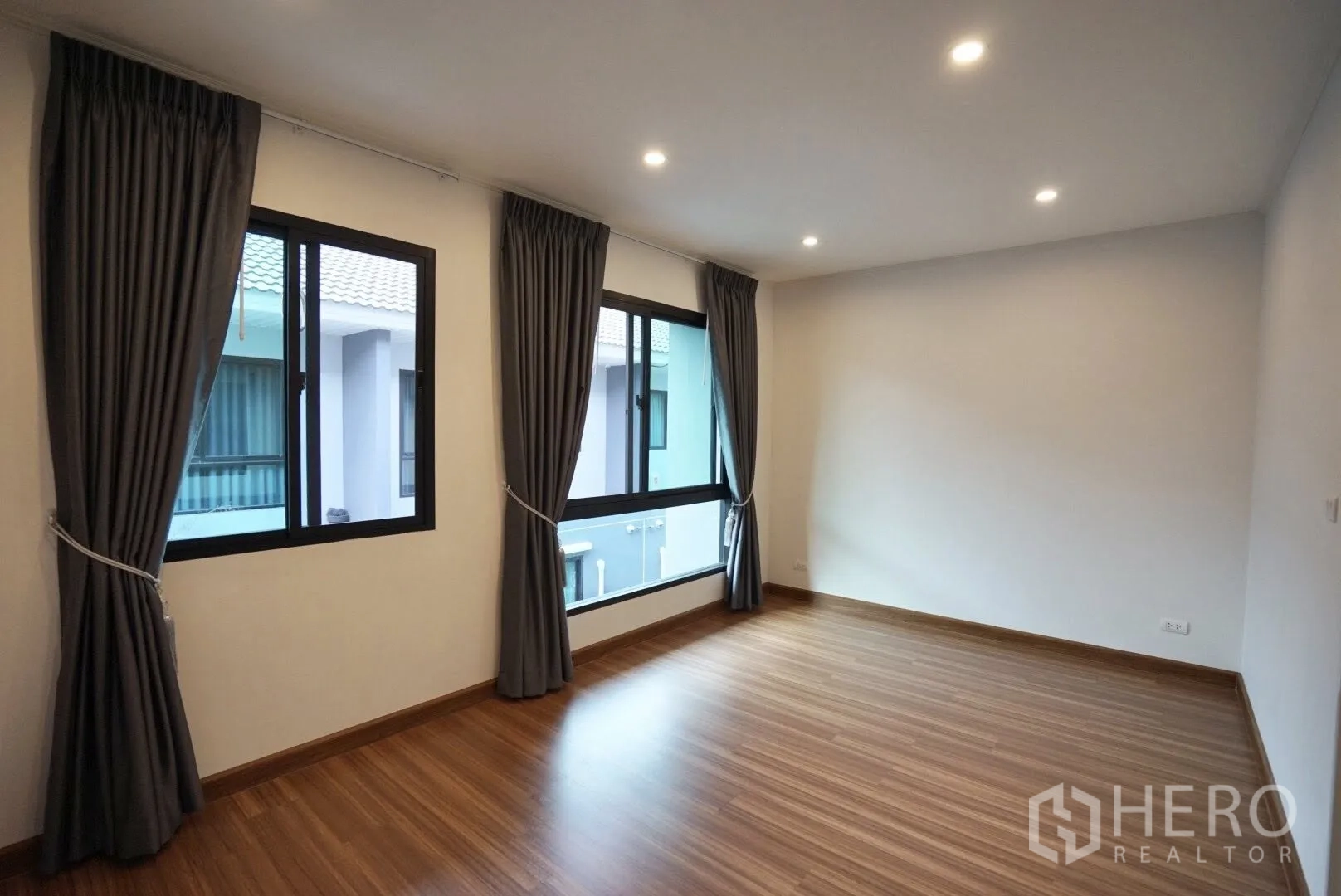 Townhouse for rent in Bang Kapi, Bangkok - Spacious empty bedroom featuring wood floors, two windows and blackout curtains.