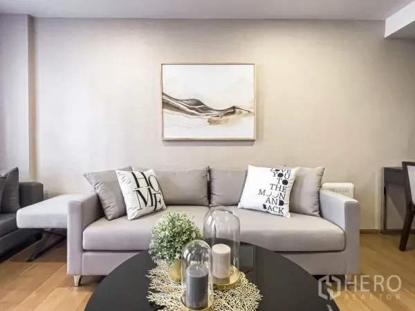 Condominium for rent in Pathum Wan, Bangkok - Bright living room featuring a gray sofa, abstract wall art, and warm wood flooring.