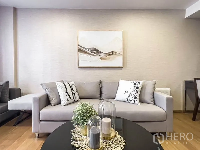 Condominium for rent in Pathum Wan, Bangkok - Bright living room featuring a gray sofa, abstract wall art, and warm wood flooring.