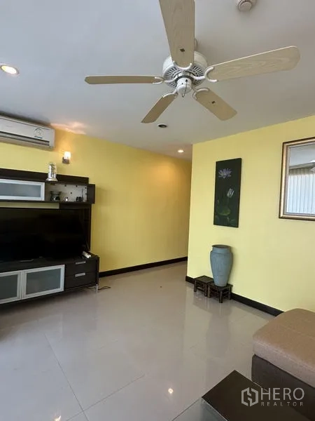 Condominium for sale in Watthana, Bangkok - Bright living room with TV console, yellow feature wall and ceiling fan.