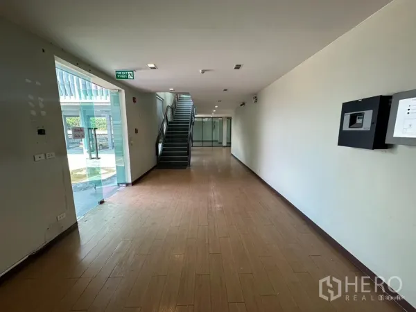 Home Office for rent in Prawet, Bangkok - Ground-floor corridor with wood-look flooring, glass entry and a staircase.