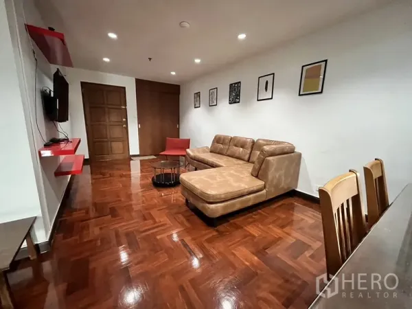Condominium for rent in Watthana, Bangkok - Living area with wall-mounted TV and red shelves facing tan sectional and dining set.