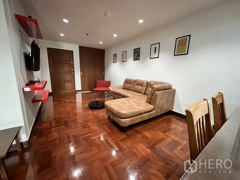 Condominium for rent in Watthana, Bangkok - Living area with wall-mounted TV and red shelves facing tan sectional and dining set.