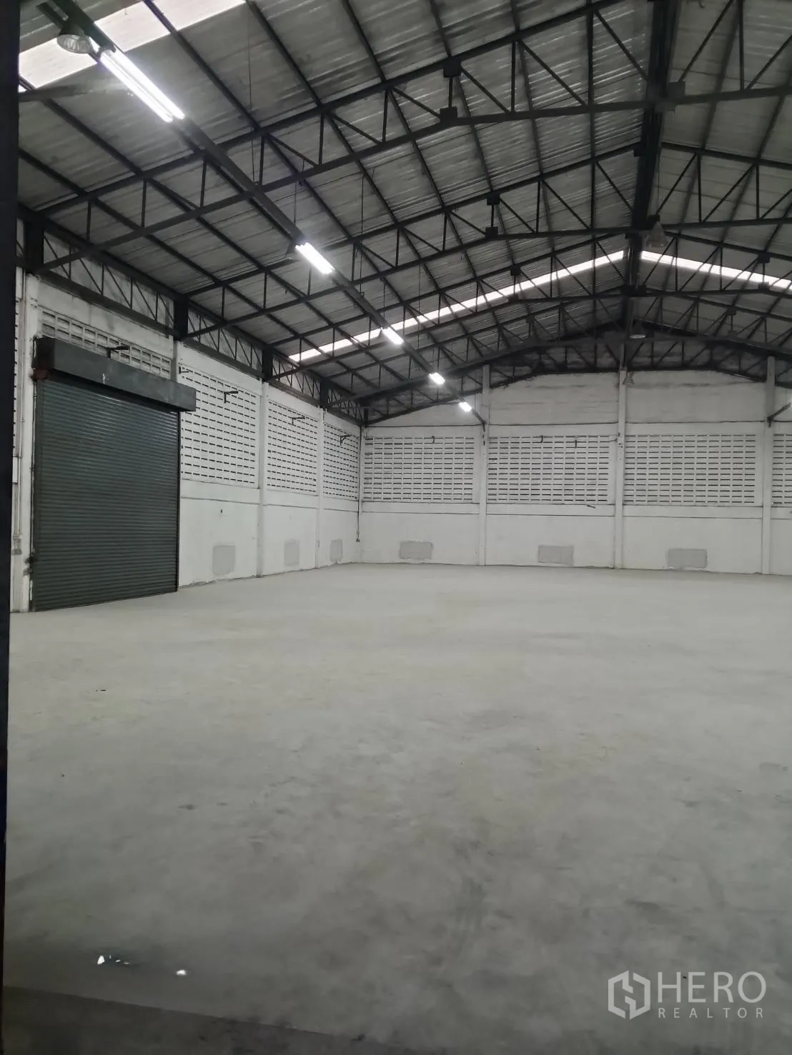 Warehouse for rent in Min Buri, Bangkok - Storage hall under steel roof trusses with bright lighting and shutter door access.