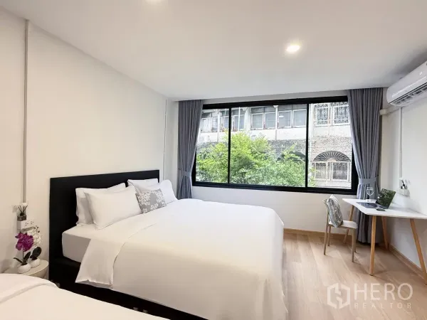 店屋 出租在Ratchathewi, Bangkok - 宽敞卧室，两张床、宽窗与工作台，眺望城市景观。