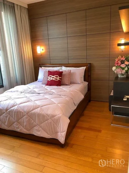 คอนโด ให้เช่า - ห้องนอนผนังไม้ มีโคมติดผนังและโต๊ะข้างพร้อมแจกันดอกไม้