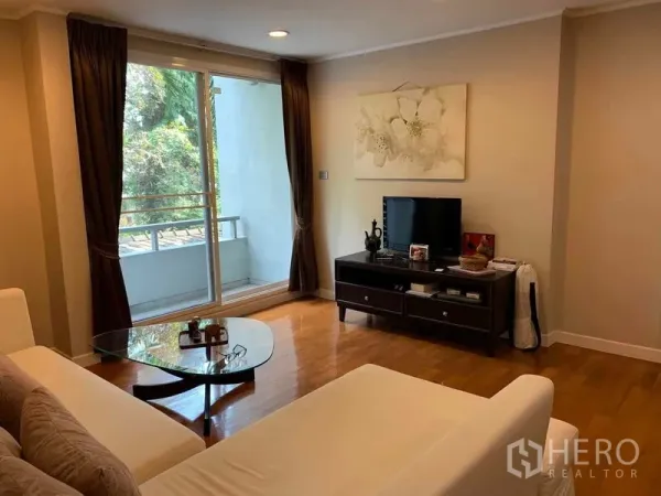 Condominium for rent in Pathum Wan, Bangkok - Cozy living room with sofa, TV console and sliding door to a balcony with greenery.