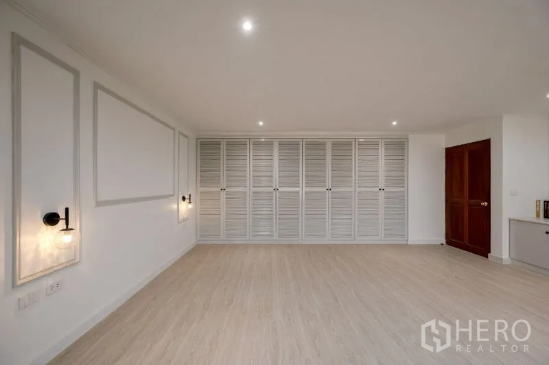 Condominium for sale - Spacious room featuring full-wall louvered closets and a wooden door.