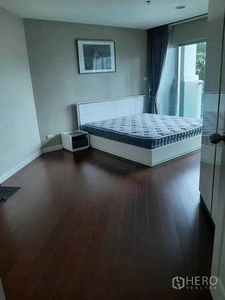 Condominium for rent or sale in Huai Khwang, Bangkok - Corner bedroom with queen bed, nightstand and access to a small balcony