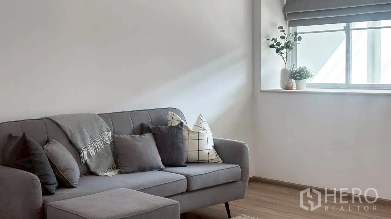 Townhouse for rent in Prawet, Bangkok - Close-up of gray sofa with layered cushions beside a window and indoor plants.