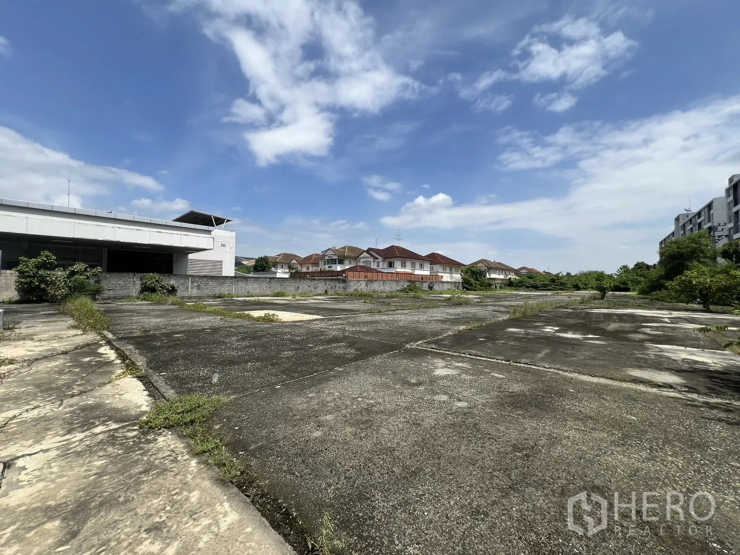 Land for sale in Bang Kapi, Bangkok - Corner of the land beside a warehouse-style building and rows of detached houses.