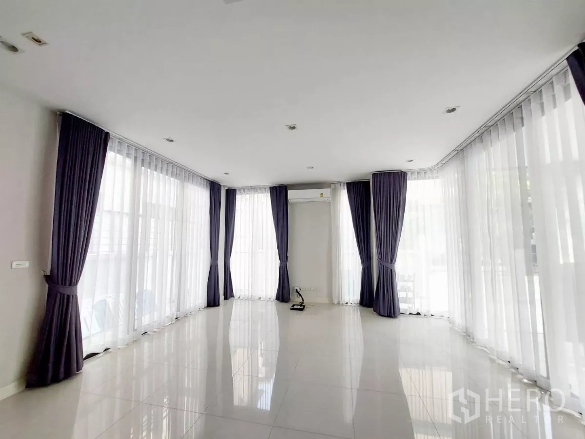 ทาวน์เฮาส์ ให้เช่าในLat Phrao, Bangkok - ห้องนั่งเล่นยาวล้อมด้วยหน้าต่างบานใหญ่ ม่านสีม่วง และพื้นกระเบื้องเงา