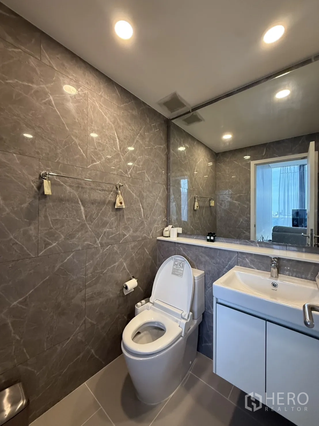 Condominium for sale in Chatuchak, Bangkok - Modern bathroom with marble-effect tiles, vanity, large mirror, and toilet.