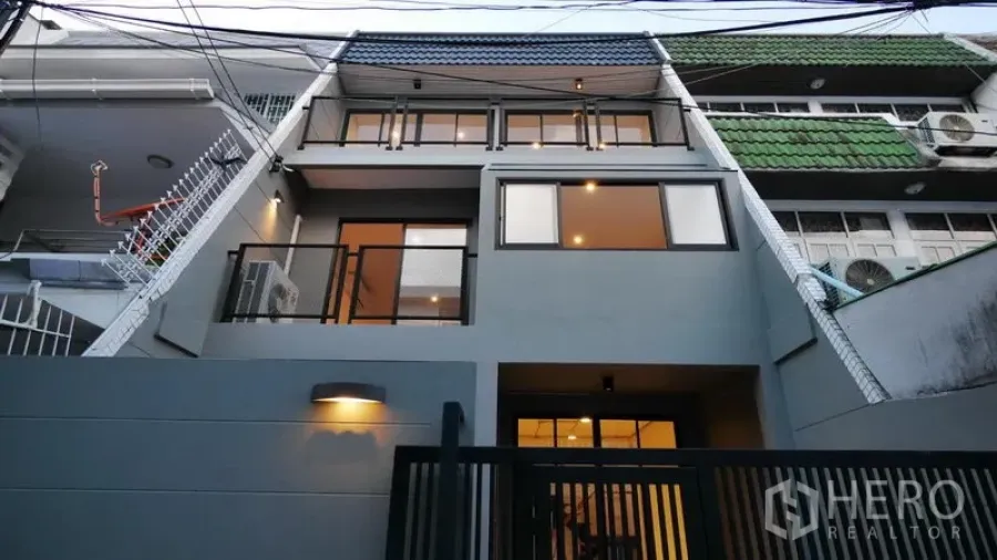 ทาวน์เฮาส์ ให้เช่าในWatthana, Bangkok - ด้านหน้าทาวน์เฮาส์ 3 ชั้น โทนสีเทา มีกำแพงและประตูรั้วสีดำ เปิดไฟสว่าง