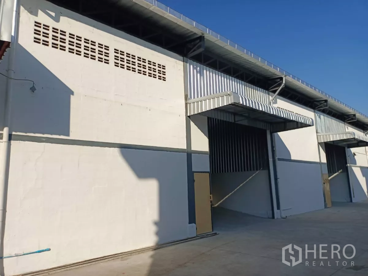 Warehouse for rent in Suan Luang, Bangkok - Row of warehouse bays with canopies and roll-up doors under a clear blue sky.