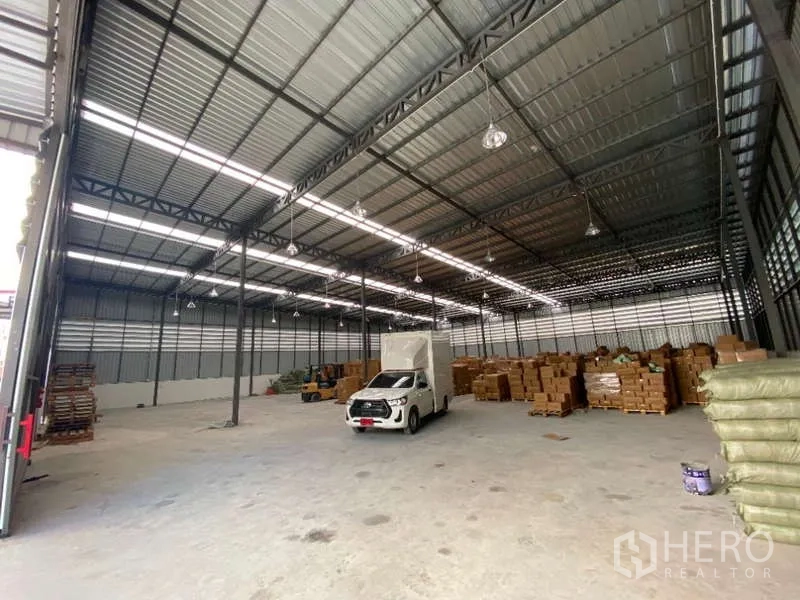 Warehouse for rent in Don Mueang, Bangkok - Spacious warehouse interior with high steel trusses, bright lighting, a small truck, and stacked cartons.