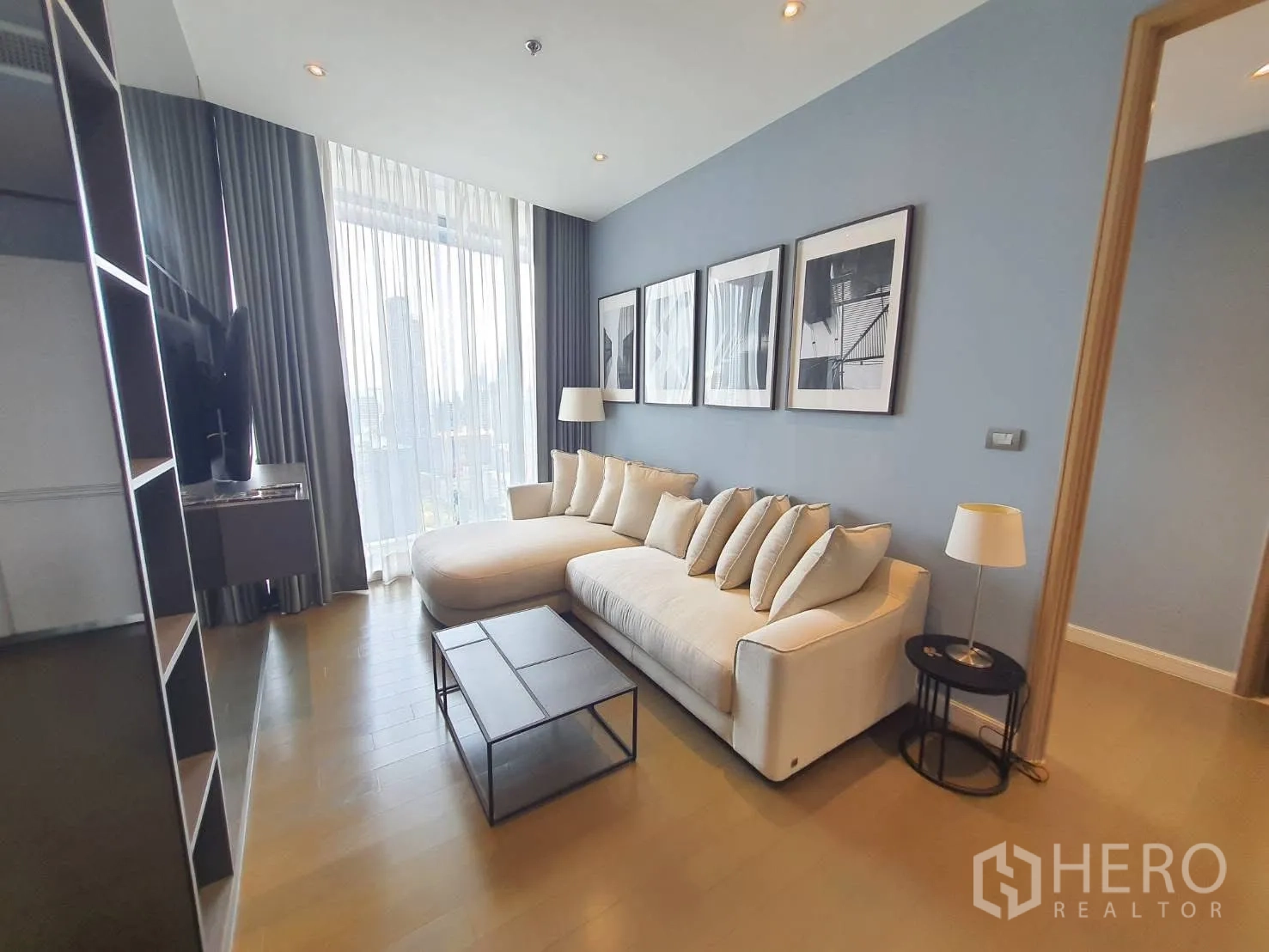 คอนโด for rent in Pathum Wan, Bangkok - ห้องนั่งเล่นสไตล์โมเดิร์น โซฟายาว สีอ่อน กรอบรูปบนผนัง และหน้าต่างสูงพร้อมผ้าม่านโปร่งวิวเมือง