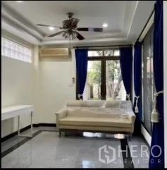 独立式住宅 出租在Phra Khanong, Bangkok - 明亮客厅，白色沙发，蓝色窗帘，吊扇与亮面地坪。